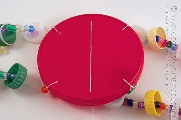 Large plastic lid threaded with string onto a large plastic lid with beads