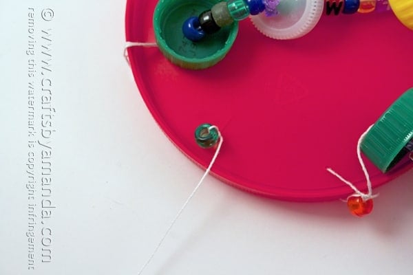 bead attached to a string threaded through a large plastic lid