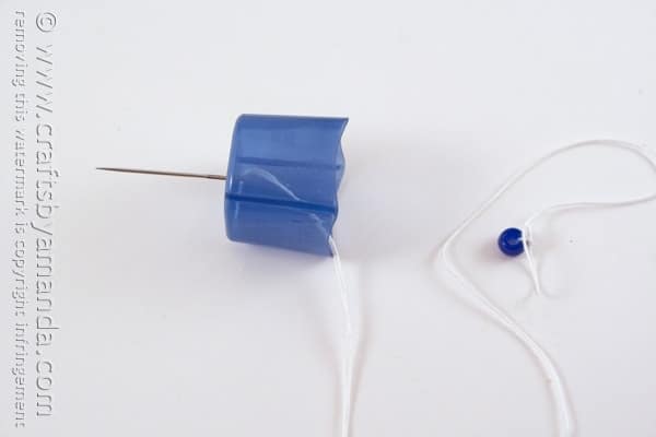 needle poked through a blue plastic lid with a string attached
