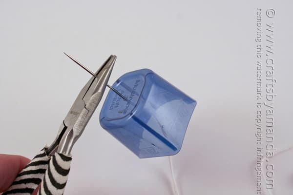 pliers pulling needle through a hole in a plastic lid