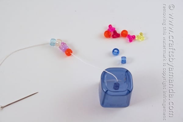 adding colorful beads to a string attached to a plastic lid
