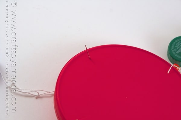 needle poking through a large plastic lid