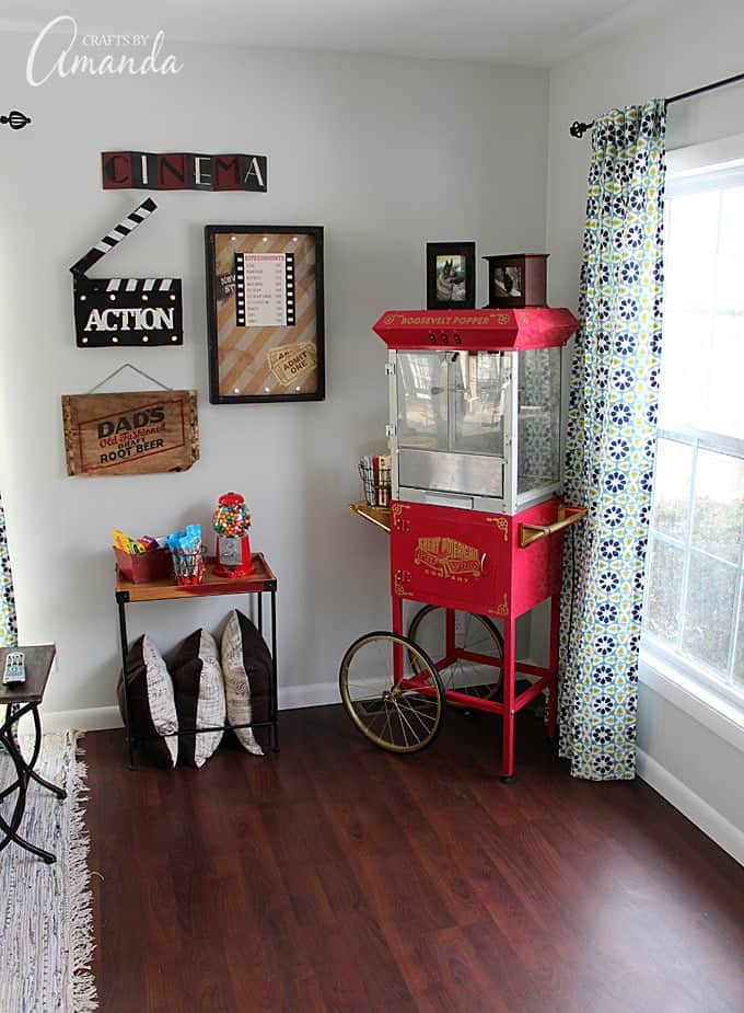 Decorate your family room with movie theater themed decor for a fun mini theater room experience! Fun movie room wall art, zombie pillows, a real popcorn maker and even candy and snacks make this room a fun place for family movie night.