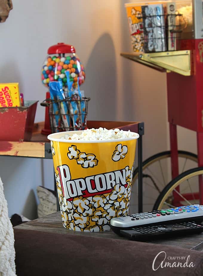 Decorate your family room with movie theater themed decor for a fun mini theater room experience! Fun movie room wall art, zombie pillows, a real popcorn maker and even candy and snacks make this room a fun place for family movie night.