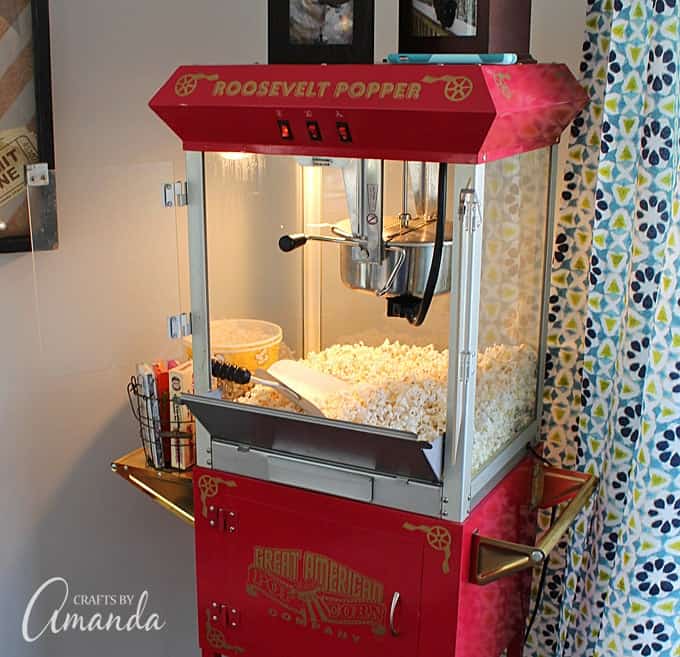 Decorate your family room with movie theater themed decor for a fun mini theater room experience! Fun movie room wall art, zombie pillows, a real popcorn maker and even candy and snacks make this room a fun place for family movie night.