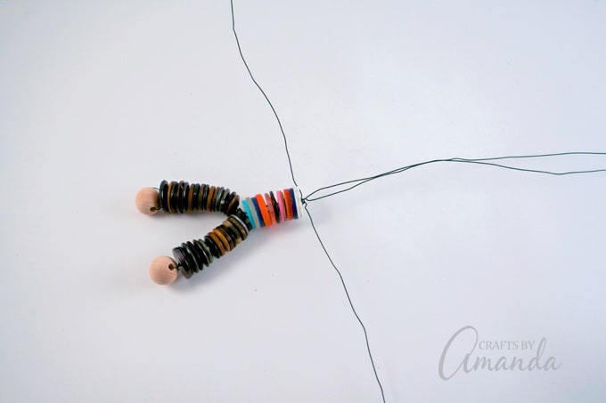 Separate the wires, one left, one right and two up. Add two buttons to the wire pointed up then add the large round bead.