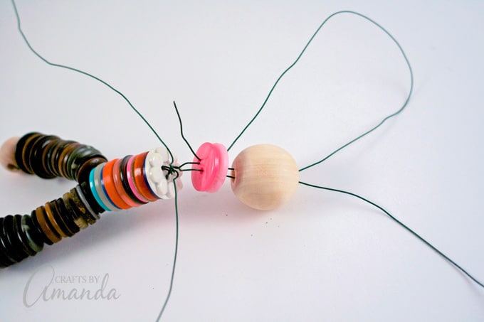 Take the wires from the top of the bead and thread them back down through the two buttons below. Do this on both sides of the bead and pull the wire all the way through.