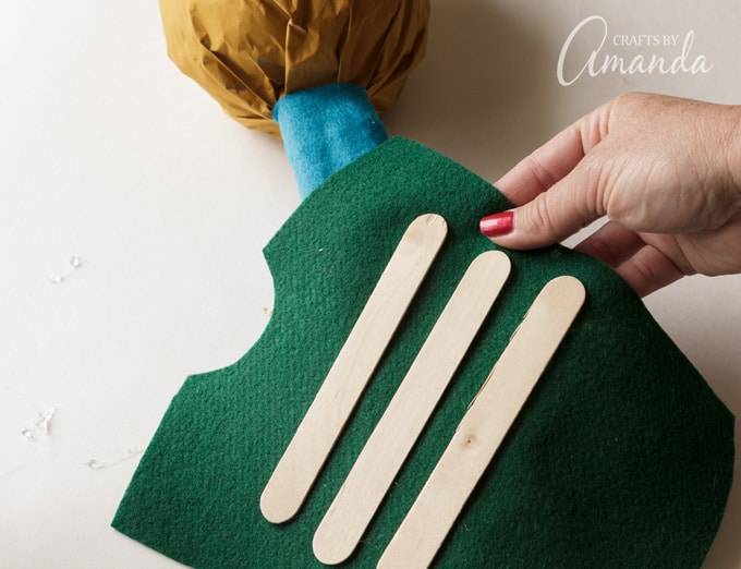 Gluing craft sticks to felt to keep the body secure on the paper bag scarecrow