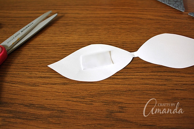 ​Roll a piece of tape, sticky side out, and place it on one side of the leaf on the back side of the paper.