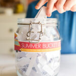 adding summer bucket list slips of paper to a jar