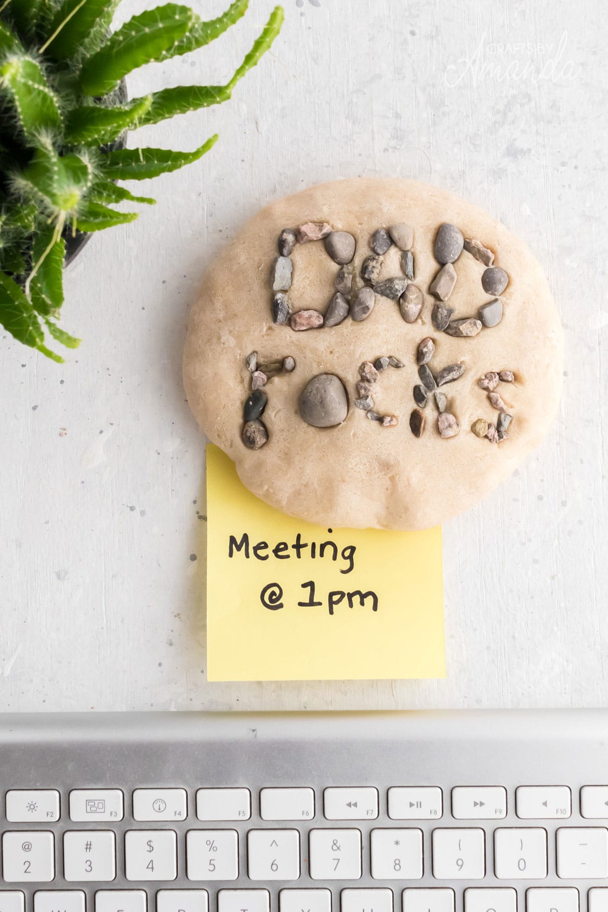 paperweight that says dad rocks on it made from salt dough and rocks with a post it under it near a computer keyboard