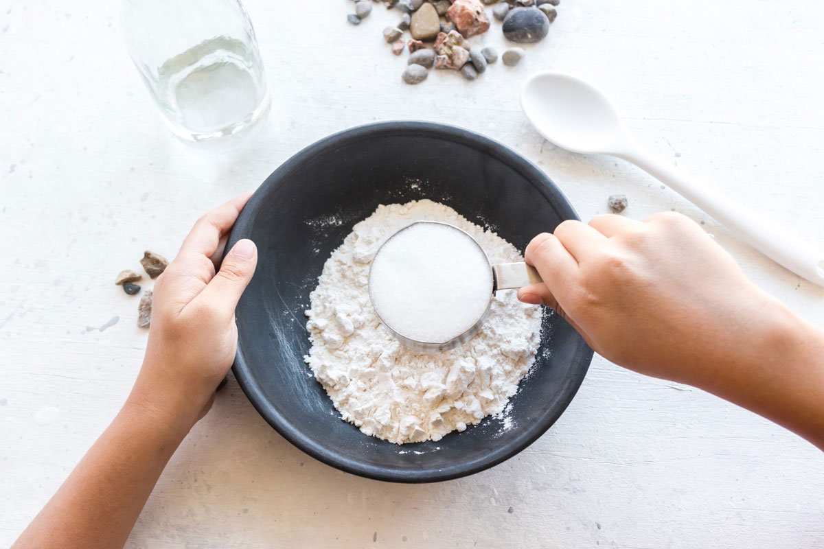 child adding flour and salt to a bowl