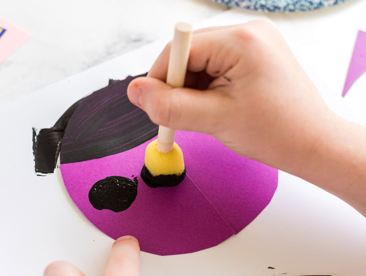child adding black paint dots to paper