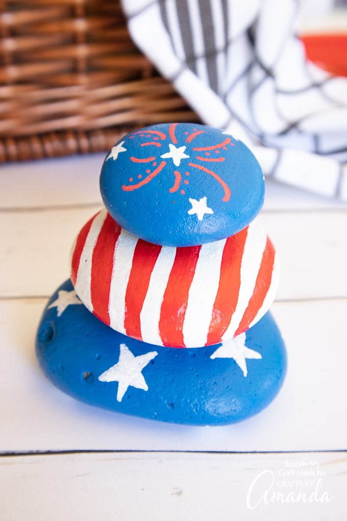 4th of july painted rocks stacked in front of a picnic basket