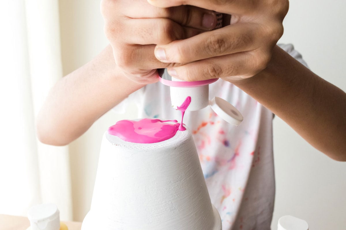 child squeezing pink paint only the bottom of a white pot