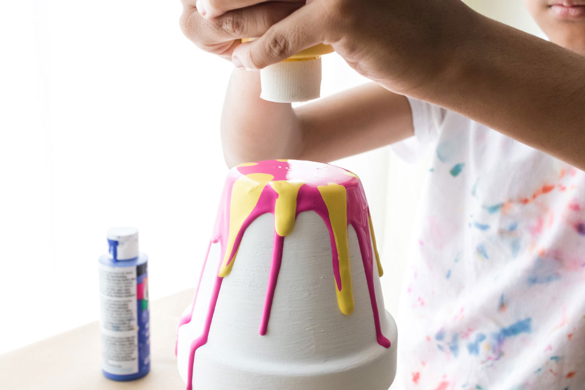 child squeezing yellow paint over pink paint