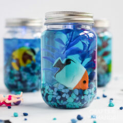 plastic jar with aquarium gravel, plastic fish, and plastic plant, in blue water