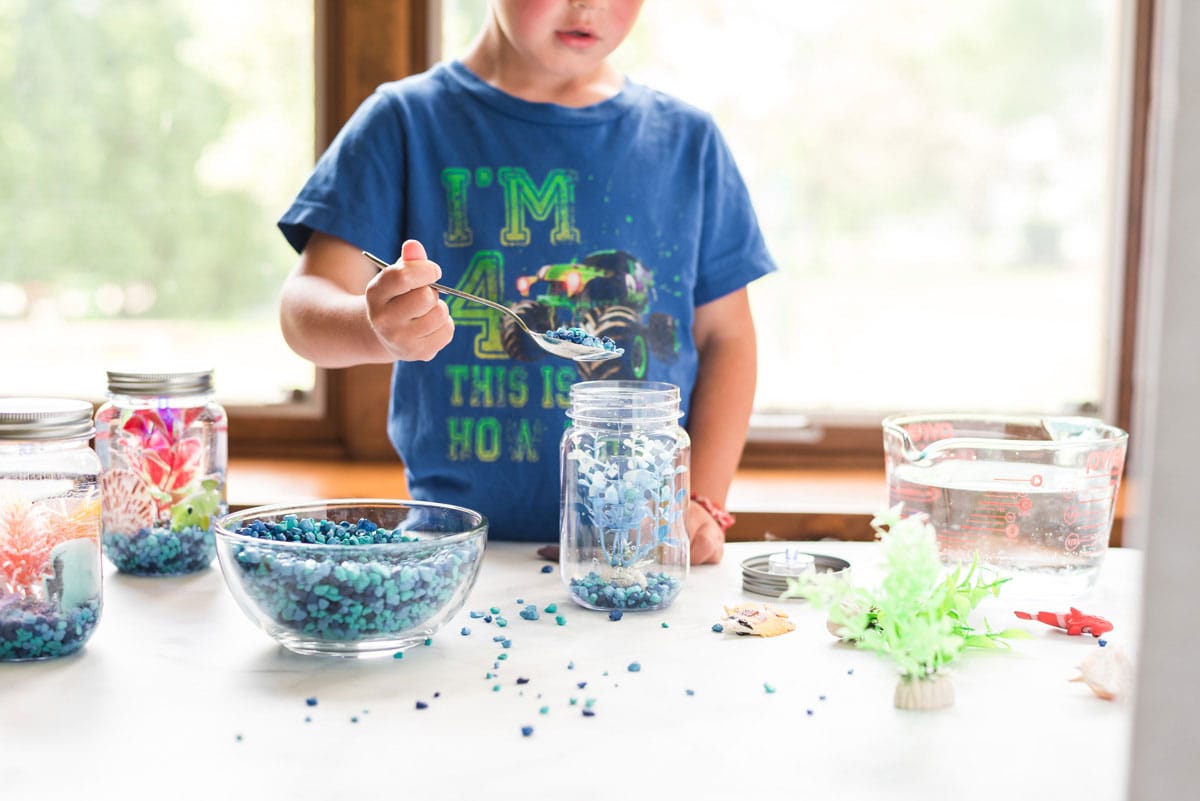 little boy adding aquarium gravel to a jar with a spoon