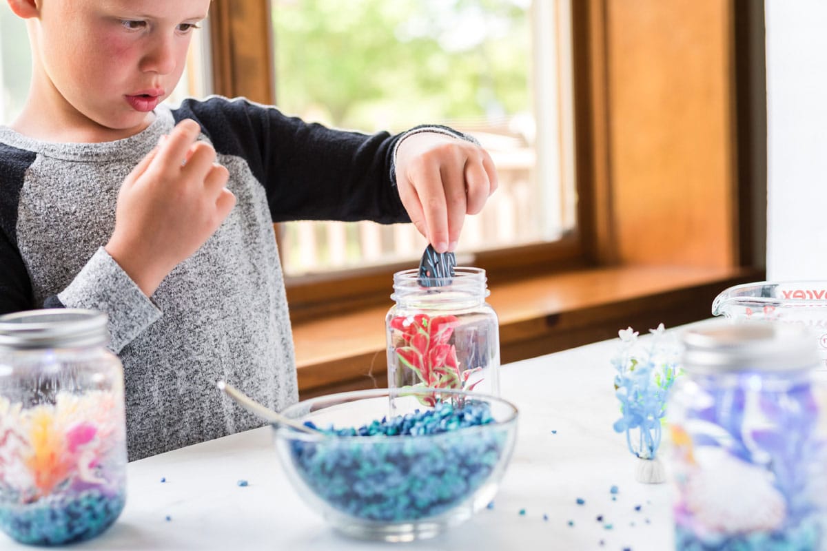 little boy adding plastic fish to jar