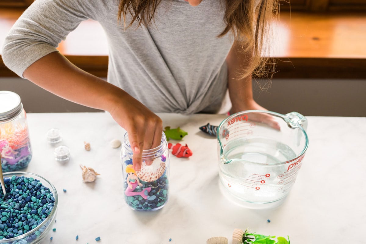 young girl adding a seashell to jar