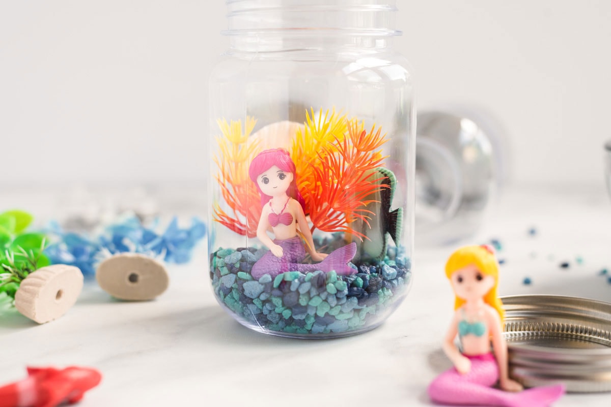 mermaid figurine with plastic plant and aquarium gravel in a glass jar