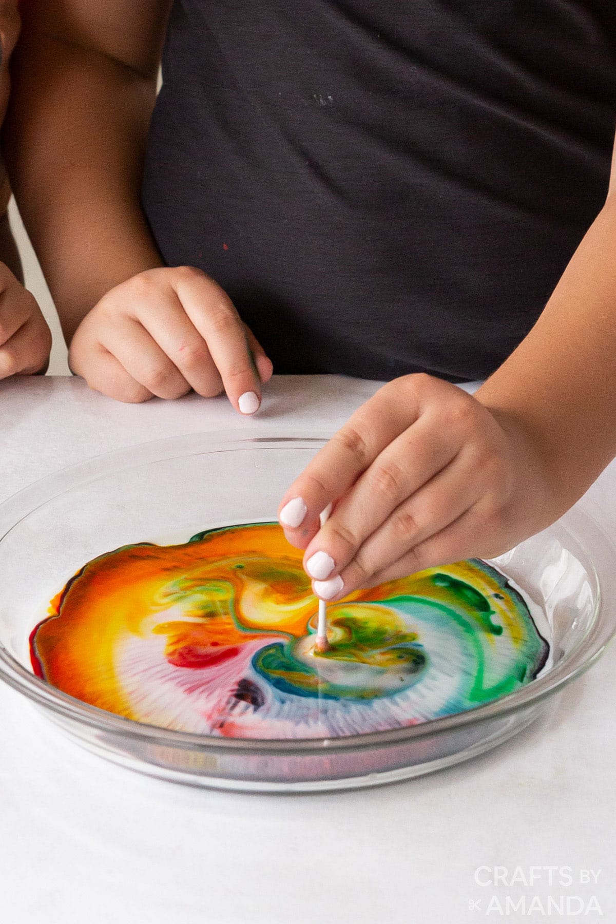 girl putting a q-tip into dish with milk and food coloring