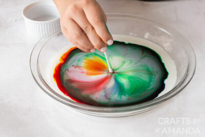 girl putting a q-tip into dish with milk and food coloring