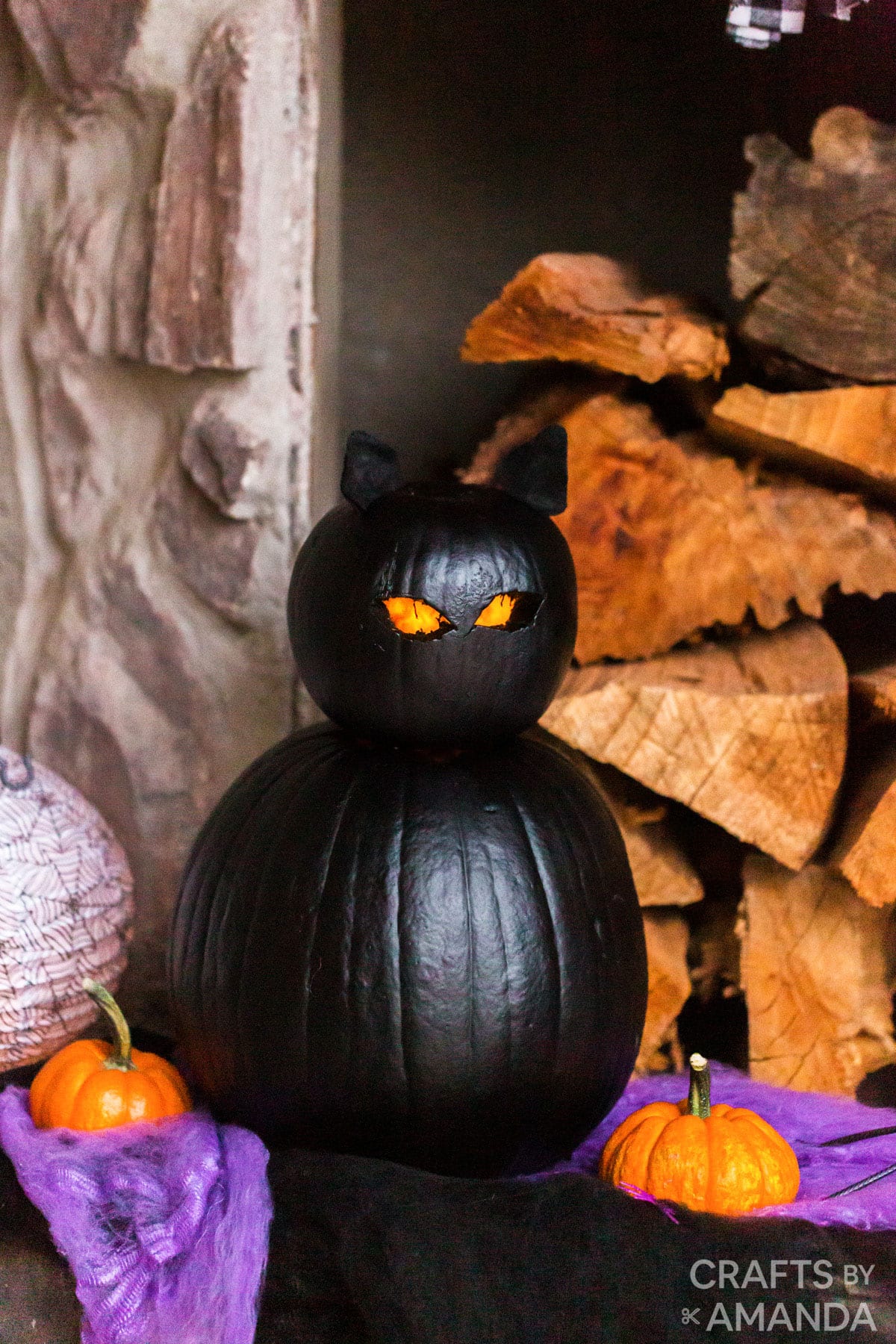 black cat pumpkin sitting near piles of wood