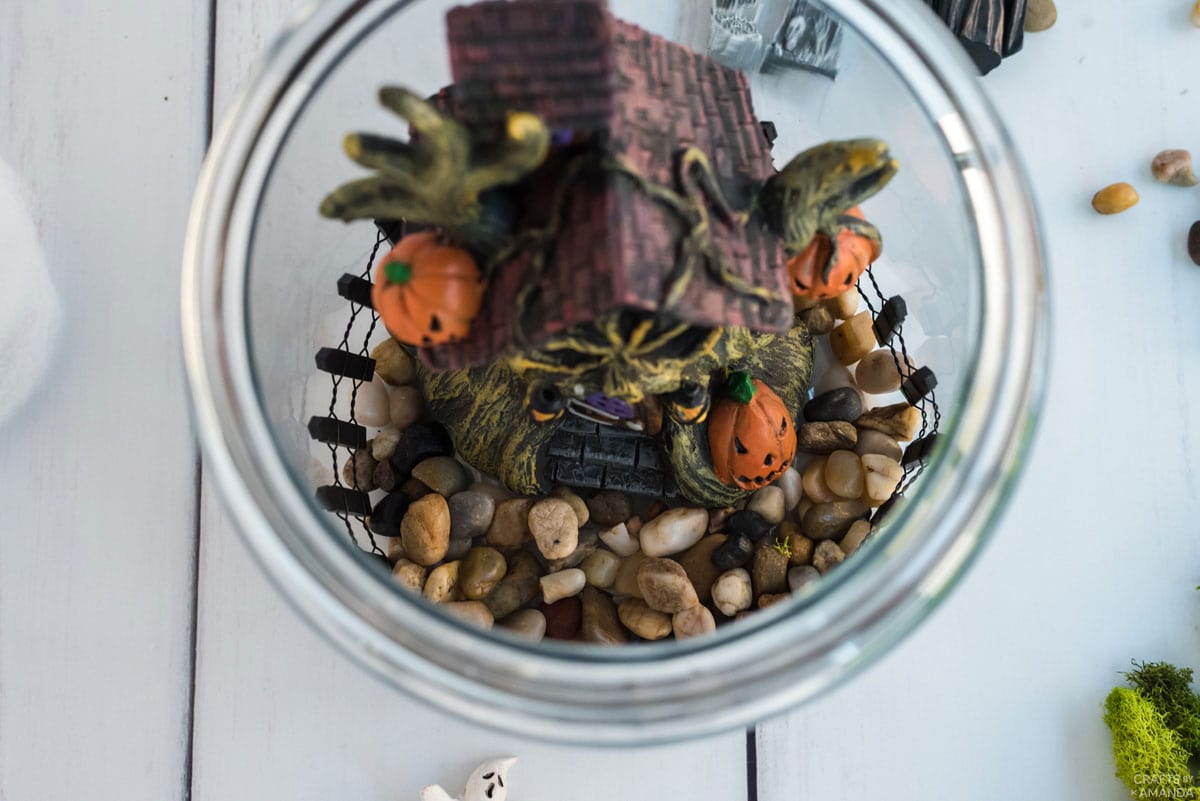haunted house figurine and pebbles inside glass canister