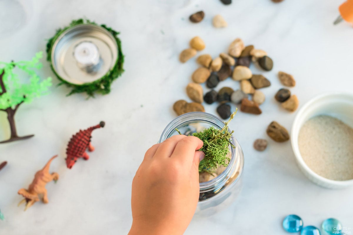 child putting moss into jar