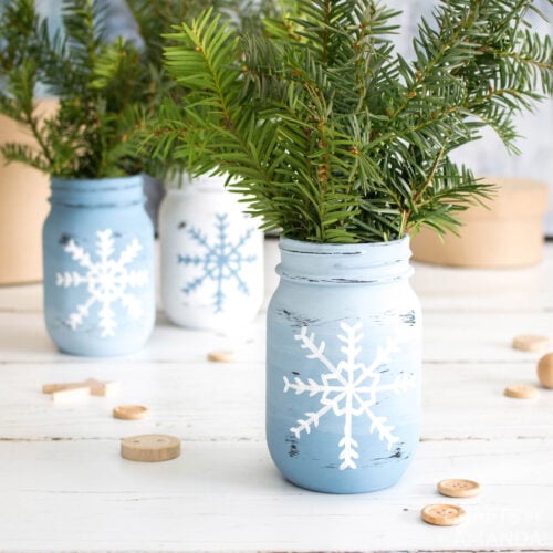 3 snowflake mason jars with sprigs on pine