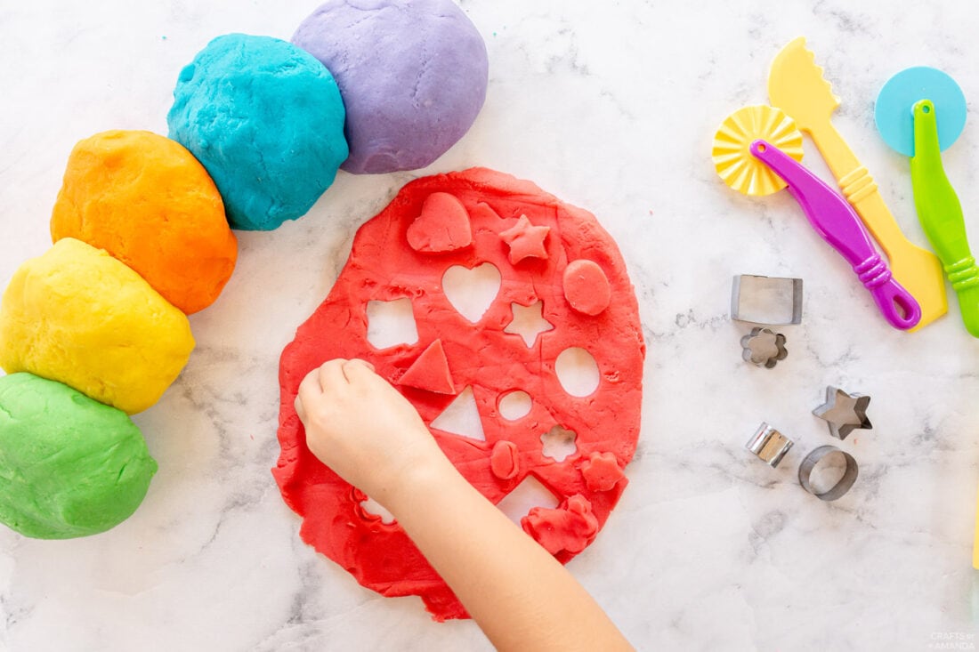 child using cookie cutter to cut out shapes from play dough