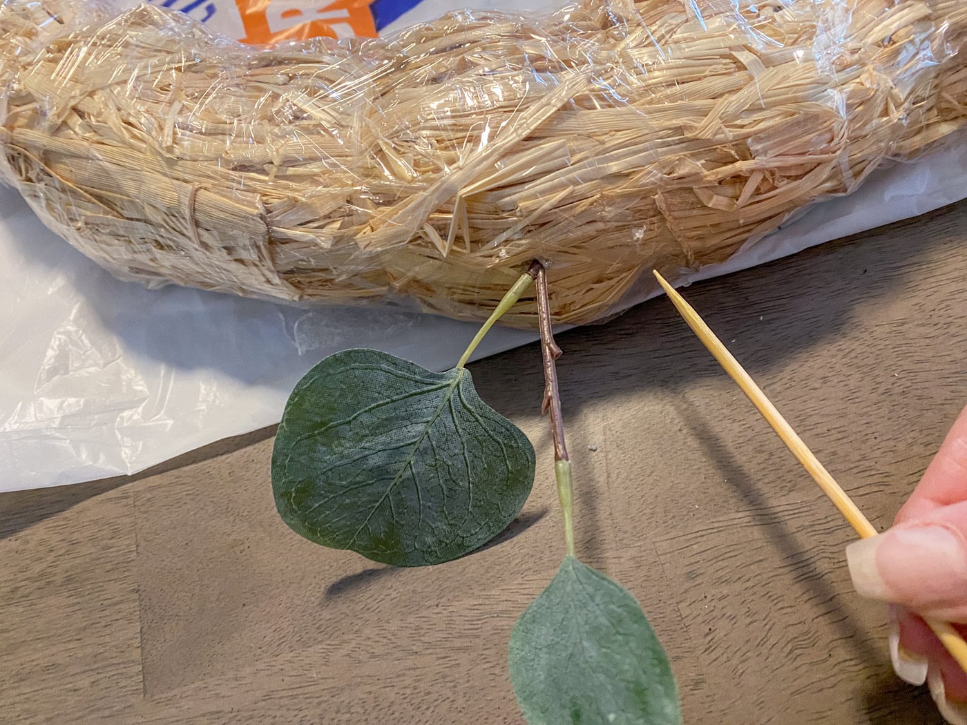 sticking faux leaf stems into straw wreath form