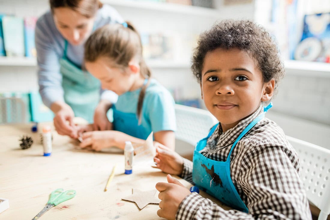 little boy looking at camera wearing an apron and making crafts